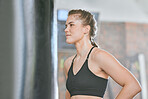 Healthy, fit and active female boxer thinking about a fight, competition or match in the gym or health club. Young woman training, exercising and working out in a fitness studio and looking dedicated