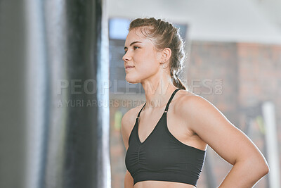 Healthy, fit and active female boxer thinking about a fight, competition or match in the gym or health club. Young woman training, exercising and working out in a fitness studio and looking dedicated