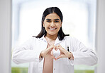 Smiling, caring medical doctor with heart sign hands gesture in modern clinic or hospital. Happy, positive and wellness young healthcare worker or physician with support and care symbol