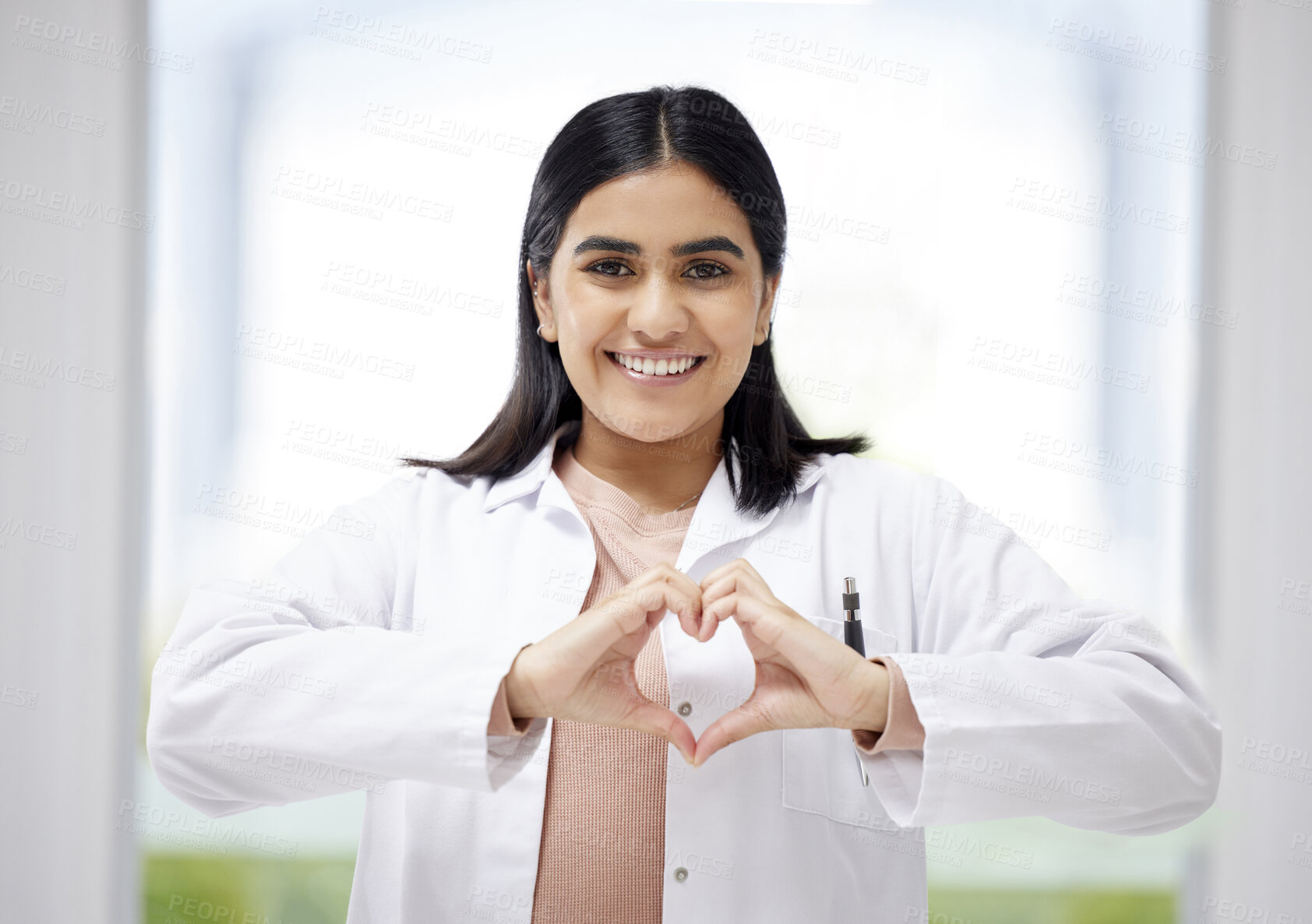 Buy stock photo Smiling, caring medical doctor with heart sign hands gesture in modern clinic or hospital. Happy, positive and wellness young healthcare worker or physician with support and care symbol