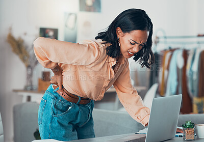 Buy stock photo Back pain, discomfort and tired designer working on a laptop in a clothing boutique or store. Young overworked business owner, shop assistant suffering from injury, backache and pain at desk