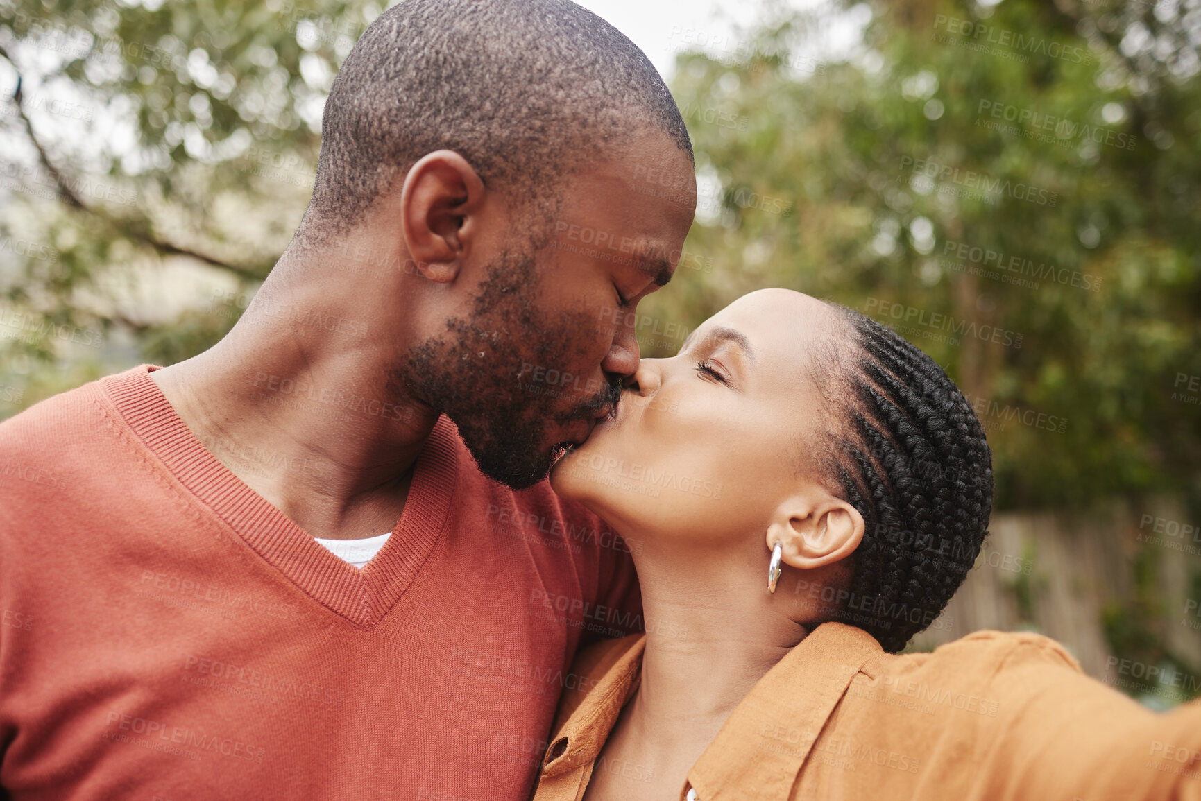 Buy stock photo Romantic, in love and young couple kissing and taking a selfie outdoors in nature on a picnic. Happy, loving and African partners taking a picture while spending quality time together in a garden.