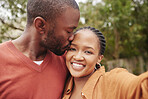 Affectionate, loving and happy couple taking a selfie while the boyfriend is kissing his smiling girlfriend on the forehead outdoors. Carefree lovers African American lovers having fun at the park