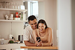 Happy, romantic and in love couple laughing at funny social media videos on her phone while relaxing together at home. Carefree, smiling and young boyfriend hugging his cute girlfriend in the kitchen
