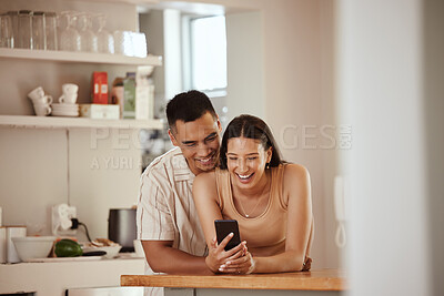 Buy stock photo Happy couple browsing on a phone and laughing at funny social media videos on her phone while relaxing together at home. Carefree, smiling and young boyfriend hugging his girlfriend in the kitchen
