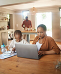 Busy, serious and multitask mother working on laptop while taking care of her child at home. Black entrepreneur or freelancer analyzing online reports with her and cute son playing games on a phone