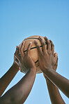 Hands holding a basketball at the start of a league match or competition against a blue sky background. Closeup of African American athletes or sportsmen playing and practicing with a ball