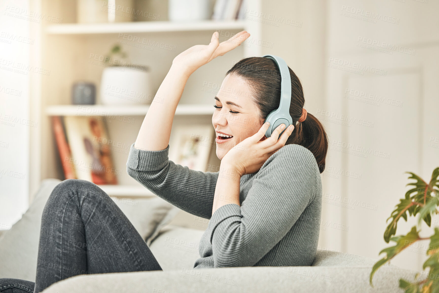 Buy stock photo Carefree, smiling and relaxed woman listening to music, singing and having fun while sitting on the couch at home.  Happy, cheerful and content female enjoying radio audio and relaxing on sofa