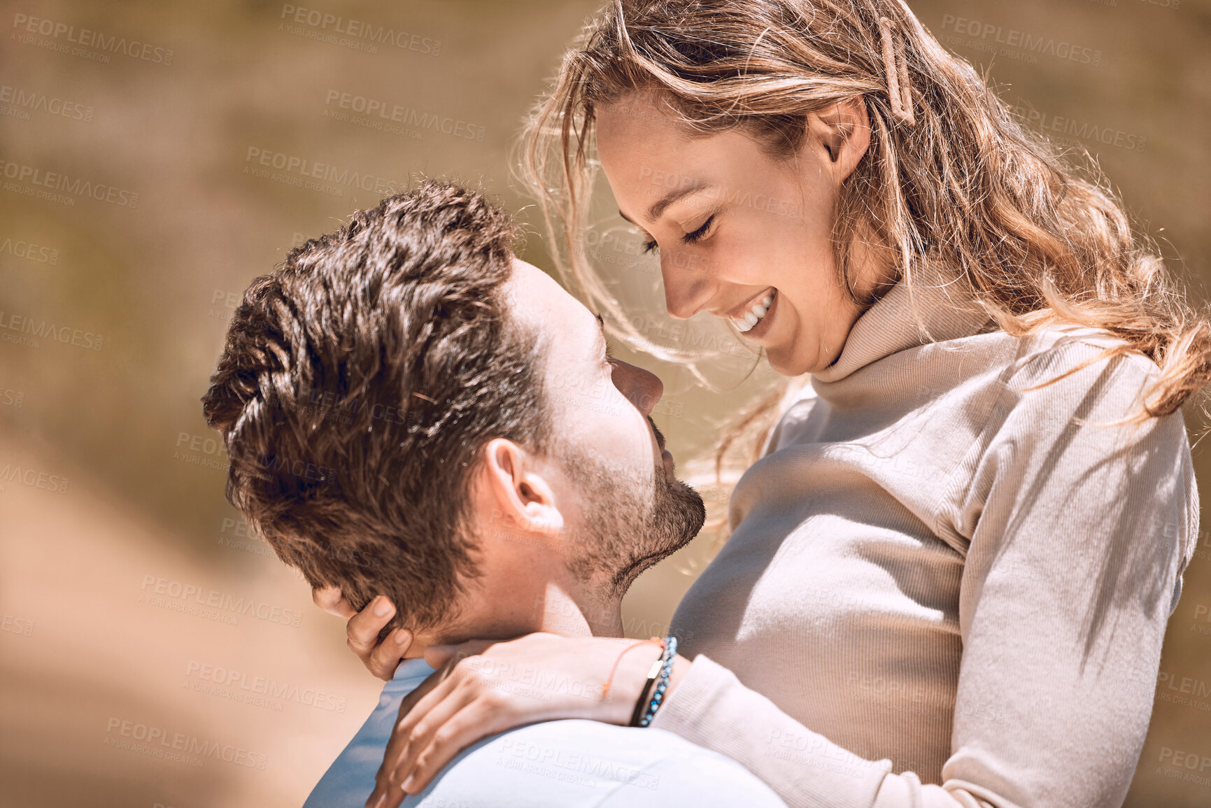 Buy stock photo Loving, affectionate and caring young couple bonding while enjoying the day outdoors in nature. Happy, in love and smiling man embracing his wife while holding her outside on a valley or hill.