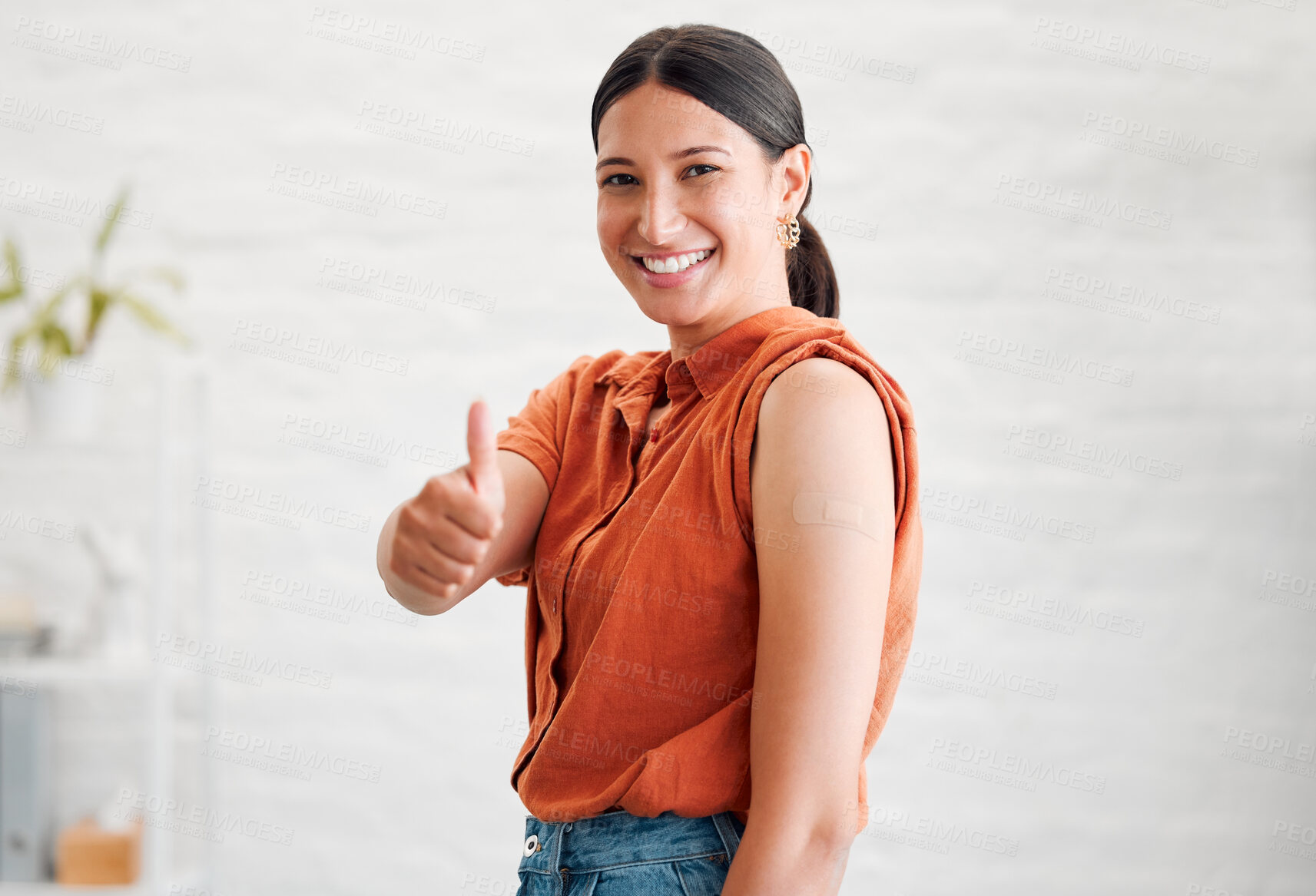 Buy stock photo Positive young woman treated with covid vaccine injection, gestures thumbs up and showing her arm to approve immunization. Happy healthy female patient wearing bandaid after her treatment shot