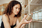 Woman in a kitchen with a spice jar preparing to cook a healthy, organic and delicious meal for lunch. Young female chef storing raw dry herbs in a glass container in her food pantry at home.