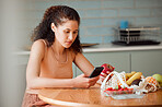 Diet, healthy living and health food of a female looking up nutrition value of an apple on a phone. Young woman at home reading online of weight loss and organic cooking holding fruit in a kitchen 
