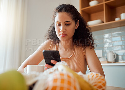 Buy stock photo Healthy, wellness lifestyle woman sitting at home kitchen table scrolling on social media on her phone during breakfast. Young female enjoying her cup of coffee while texting in the morning