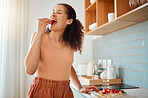 Eating, chopping and making fruit salad with strawberries, bananas and healthy ingredients in home kitchen. Woman biting, tasting and snacking on fresh vitamins while cooking and preparing breakfast