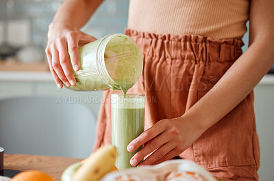 Buy stock photo Woman pouring healthy smoothie in a glass from a blender jar on a counter for detox. Female making fresh green fruit  juice in her kitchen with vegetables and consumables for a fit lifestyle.