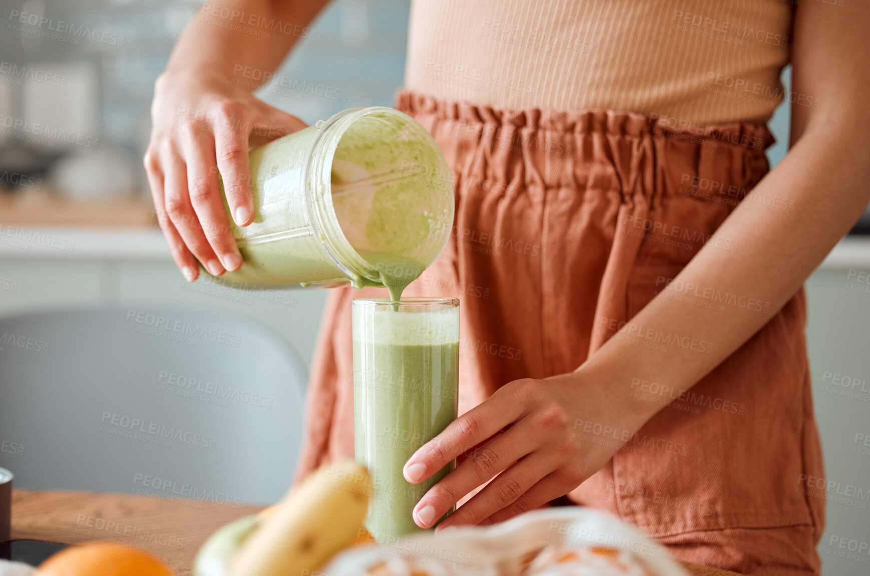 Buy stock photo Woman pouring healthy smoothie in a glass from a blender jar on a counter for detox. Female making fresh green fruit  juice in her kitchen with vegetables and consumables for a fit lifestyle.