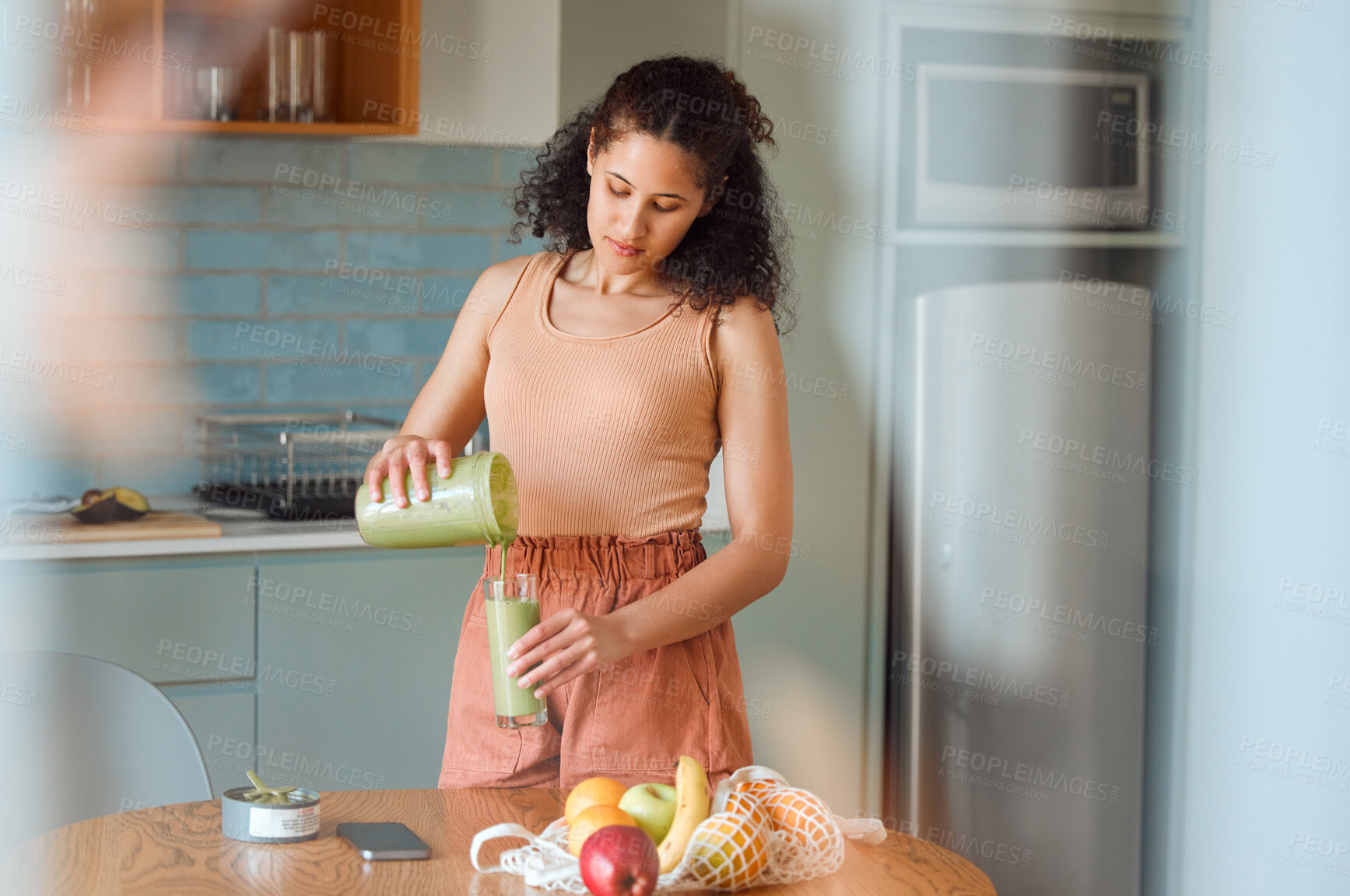 Buy stock photo Healthy, nutrition and wellness smoothie made by young woman for her fresh, green detox or vegan diet at home in her kitchen. Vegetarian female pouring and drinking her organic homemade fruit juice 