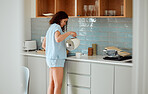 Young woman having coffee, tea or morning routine in comfortable pajamas in her stylish kitchen at home. Millennial girl starting her day with caffeine or beverage using latest appliance in apartment