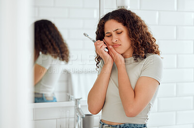 Buy stock photo Toothache, pain and sensitive teeth with a woman brushing her teeth in a bathroom at home. Young female with a cavity suffering from discomfort during dental hygiene routine. Lady with a sore mouth 