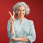 Senior woman express peace sign, v gesture and emoji with fingers on red studio background. Portrait of carefree, cool and smiling lady in positive, playful and fun mood showing victory with hand