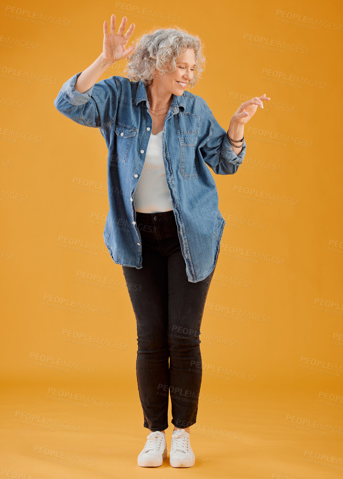 Buy stock photo Fun, happy and cheerful woman dancing, celebrating and enjoying life alone against an orange background. Senior woman feeling excited, joyful and playful with dressed stylish, trendy and fashionable