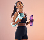 Happy, fitness and healthy woman while holding exercise mat and water bottle against peach studio background. Fit woman with slim body after exercise , training and sports workout and healthcare