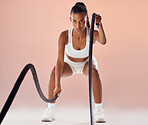 Fit woman doing cardio workout with ropes, exercising for fitness training and looking sporty while posing against a pink studio background. Active and young female athlete doing routine exercise