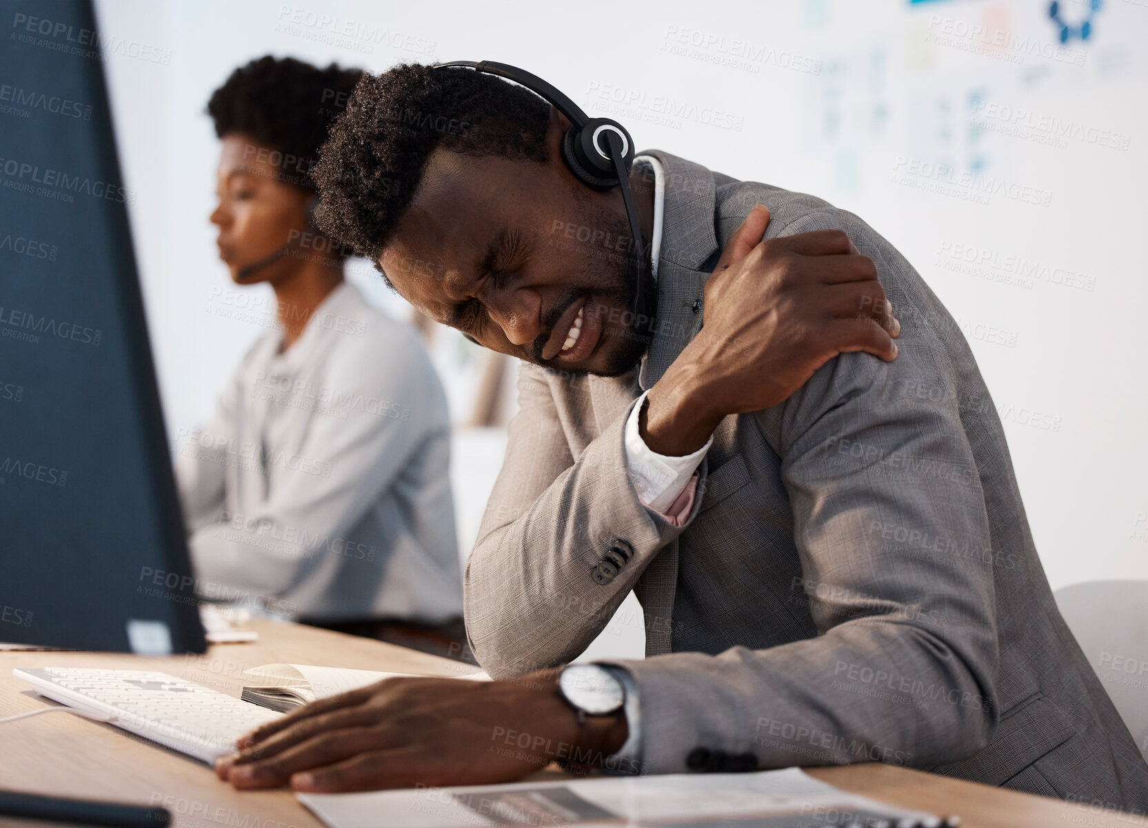 Buy stock photo Pain, injury and hurt call center agent holding his shoulder in agony while working in the office. Young African American male customer service consultant suffering from a painful arm