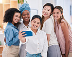 Diverse businesswomen taking selfies on a phone together in an office. Happy and beautiful female colleagues smiling for photos, posing as a dedicated and ambitious team in a creative startup agency