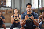 Fit, active and serious male gym instructor leading a workout session at a fitness club. Portrait of a young personal trainer or coach squatting with a kettlebell and training a group of people