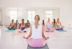 Women with instructor meditating in lotus pose with mudra hand gesture during fitness class in a yoga studio. Back of Calm or relaxed ladies sitting and praying quietly for inner peace or zen energy