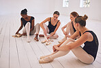 Fitness, training and the art of dance, a group of smiling young ballet dancers sitting on the floor after workout. Happy and tired ballerina girls relax, talking and sharing ideas in dancing studio