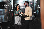 Wine production workers using alcohol machine or distillery equipment in warehouse winery. Business sommelier expert woman and man talking and working on quality control maintenance with a checklist