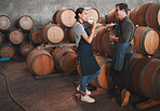 Wine distillery owners tasting the produce in the cellar standing by the barrels. Oenologists or sommeliers drinking a glass of chardonnay or sauvignon blanc inside a winery testing the quality