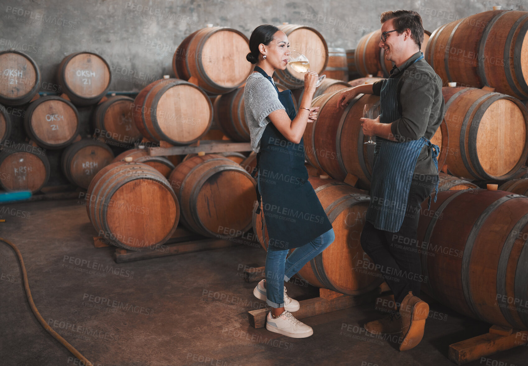 Buy stock photo Wine distillery owners tasting the produce in the cellar standing by the barrels. Oenologists or sommeliers drinking a glass of chardonnay or sauvignon blanc inside a winery testing the quality