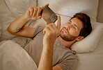 Young man relaxing in bed with phone watch, movie, series or online social media videos on an app. Browsing the internet news with 5g technology on cellphone or smartphone play a game in the bedroom