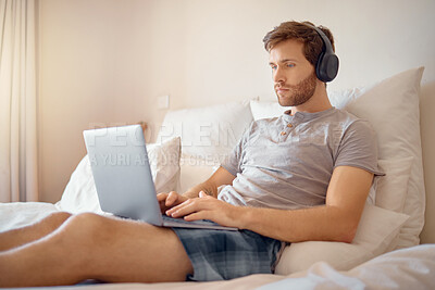 Buy stock photo Man working or typing on laptop and listening to music with headphone in bed at home. Remote worker streaming podcast online while reading and send work email on wireless tach in the bedroom alone