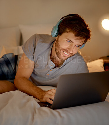 Buy stock photo Typing, headphones and in bed on laptop young man looking for movie or video to watch and relax at night in home. Happy male on internet and listening to music on streaming website and social media