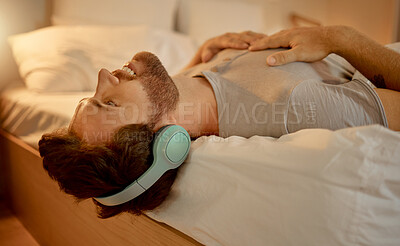 Buy stock photo Happy man, streaming a podcast in bed smiling with headphones at home. Young guy listening to music from spotify on internet or radio in earphones, time to relax, enjoy peace in his apartment bedroom