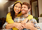 Happy, excited and interracial couple hugging looking away relaxing and sitting on a couch at home. Relaxed diverse lovers smiling and enjoying quality time together and having fun in the house