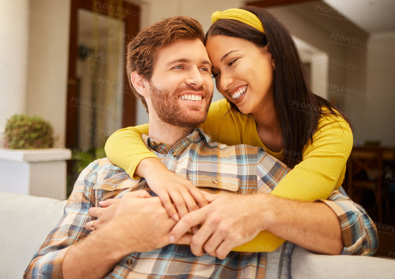 Buy stock photo Diversity, love and happy couple in living room sofa together, sharing intimate moment at home. Freedom, smile and relax young married man embracing woman bonding on marriage anniversary 