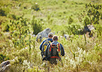 Men hiking green nature or a forest on a sunny summer day near trees and field. Active and fitness friends trekking or walking while on an adventure in the woods in a sustainable ecology environment