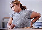 Corporate employee suffering from back pain while working at a desk in an office, uncomfortable and concerned. Young professional experience discomfort from an injury, bad posture or hurt muscle