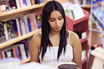 Student, book and woman reading in a library at university, college or school campus alone for education. Bookshelf, knowledge and scholarship girl student studying academic, smart and information
