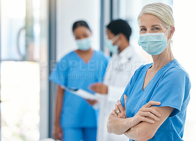 Buy stock photo Success, healthcare and leadership, woman doctor in surgical mask and scrubs, standing arms crossed with coworkers talking in background. Proud, professional and motivated to fight covid at hospital.