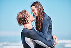 Love, surf and summer with a couple hugging on the beach with the sea or ocean in the background after surfing. Romantic young man and woman embracing face to face under a blue sky during the day