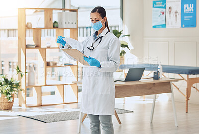 Buy stock photo Medical doctor with a clipboard and face mask in her office reading covid results during pandemic. Young healthcare employee doing hospital paperwork in the clinic room in a medicare surgery center.
