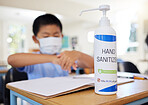 Boy rubbing hand sanitizer for hygiene, safety and protection against covid at school. Closeup bottle of alcohol gel on desk in classroom to clean, kill or prevent the spread of germs or coronavirus