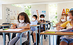 Young kids learning in classroom after covid pandemic, wearing protective face masks. Little children sitting in school with raised arm to ask questions and studying for their education