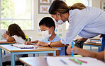 Education, covid and learning with face mask on boy doing school work in classroom, teacher helping student while writing in class. Elementary child wearing protection to stop the spread of a virus